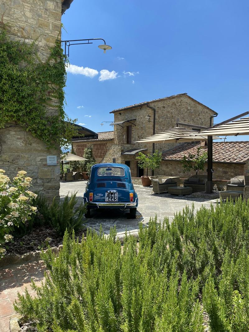Casa rural toscana de piedra con romero y un coche antiguo